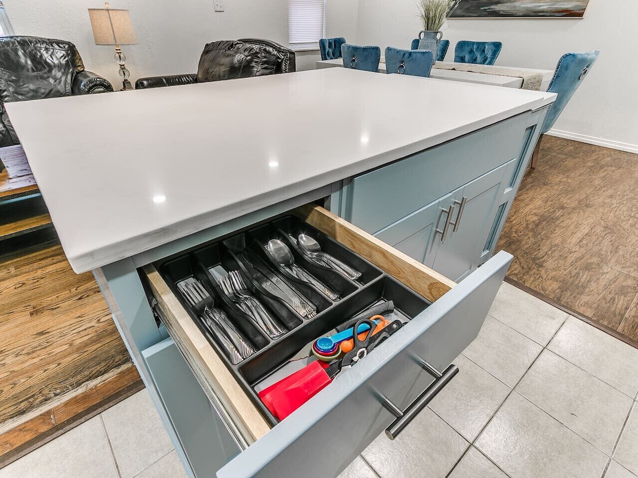 A kitchen with a white countertop, blue cabinets, and a drawer organizer containing utensils.
