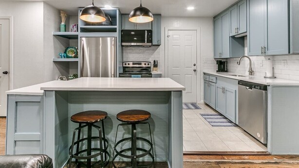 A modern kitchen with a central island, bar stools, stainless steel appliances, and light blue cabinetry. - Beautiful 2-Bedroom Near Wheeler (Oklahoma City)