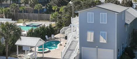 A residential building with a pool, a covered patio, and a staircase leading to a garage.