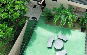 Eine Dachterrasse mit grüner Bodenfläche, umgeben von üppiger Bepflanzung und einer Treppe.