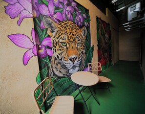 Ein Wandgemälde zeigt einen Leoparden mit violetten Blumen, einen grünen Teppich und zwei Stühle.