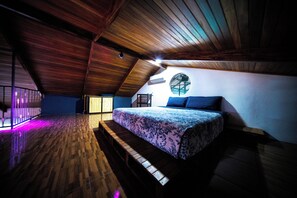 Quarto com teto de madeira, cama com colcha estampada e janela redonda.
