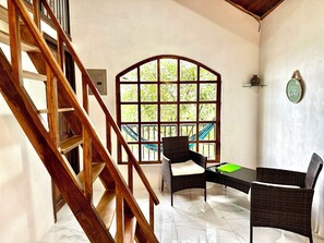 Ein Zimmer mit einer Holztreppe, einem großen Bogenfenster mit Blick auf Grünflächen, einem Korbtisch mit Stühlen und einer an der Wand befestigten Dekorplatte.