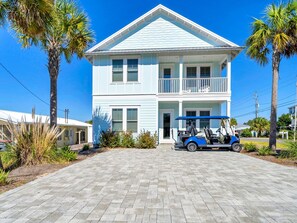 A two-story building with a light blue exterior, a balcony on the second floor, and a paved driveway. - Salty Blue (Panama City Beach)