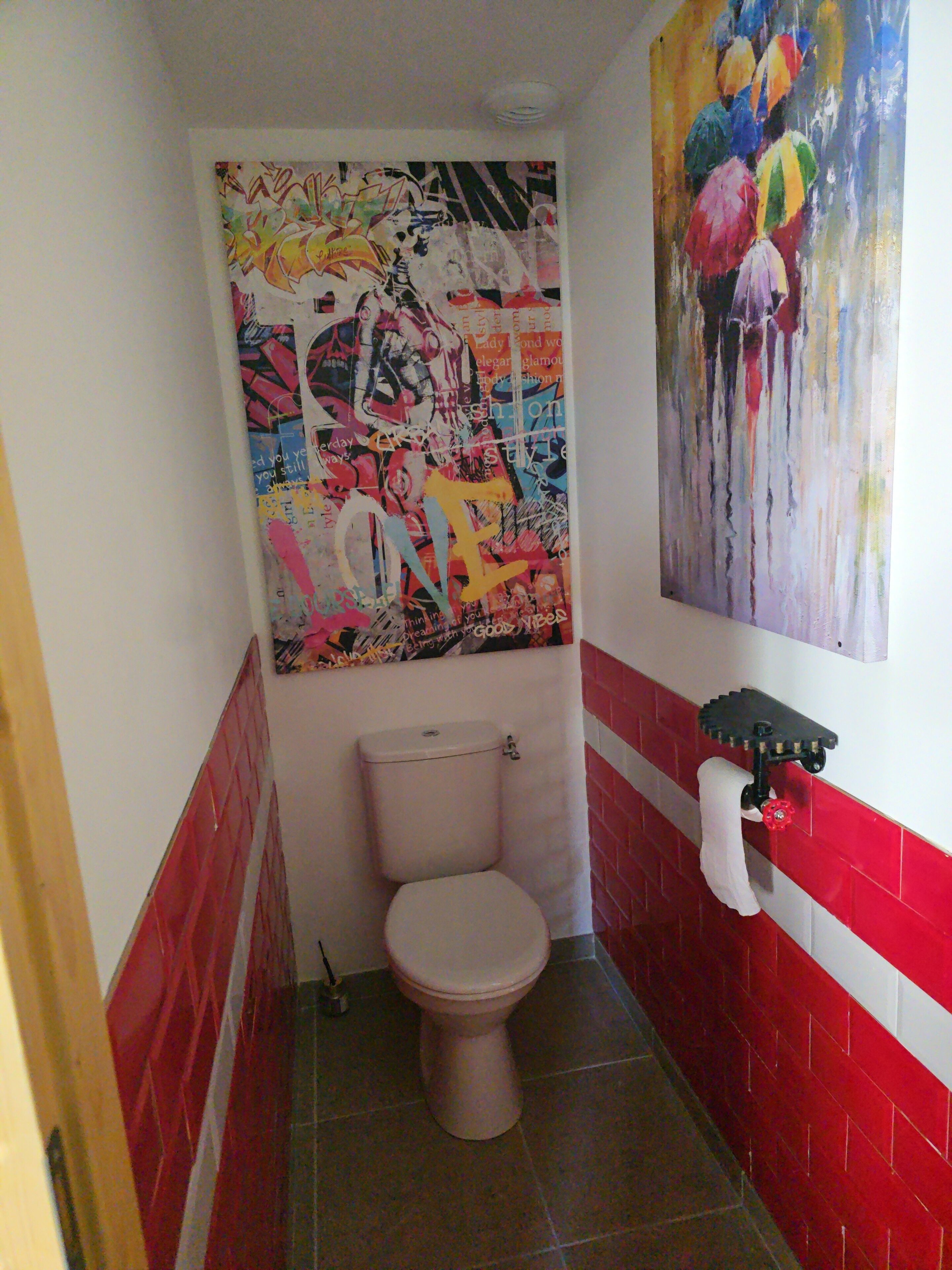 Une salle de bain avec des toilettes, un lavabo fixé au mur et un grand tableau abstrait.