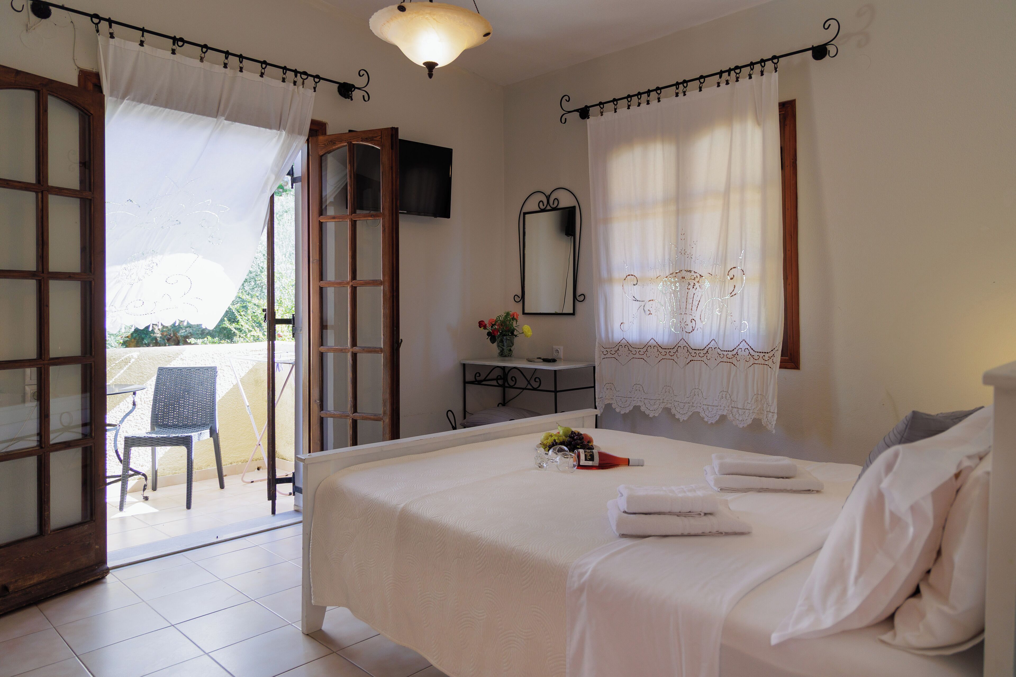A bedroom with a bed, a bedside table with a mirror, a window with curtains, and a view of the outside.