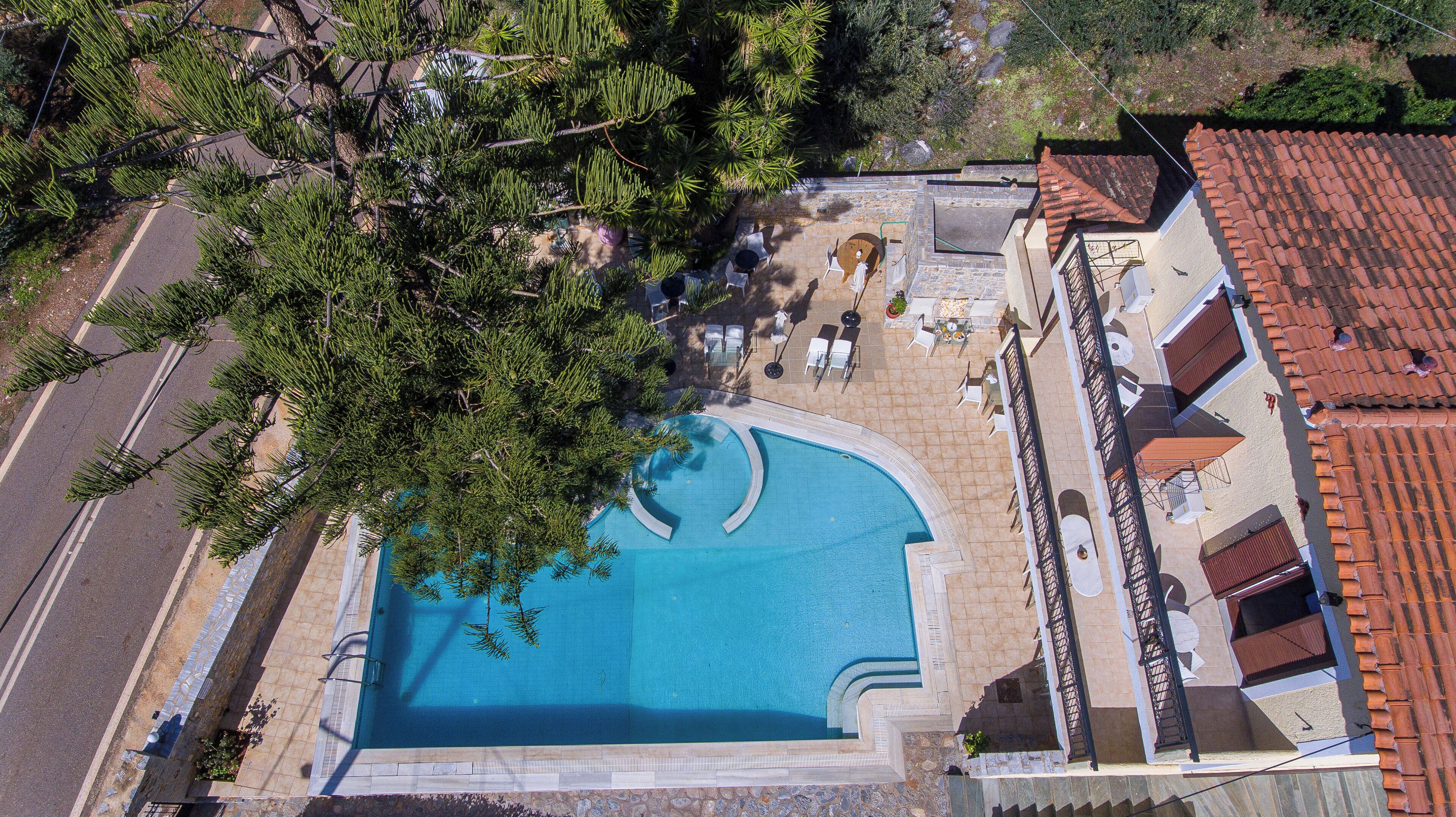 An aerial view of a resort with a large swimming pool, outdoor seating, and a tiled roof.
