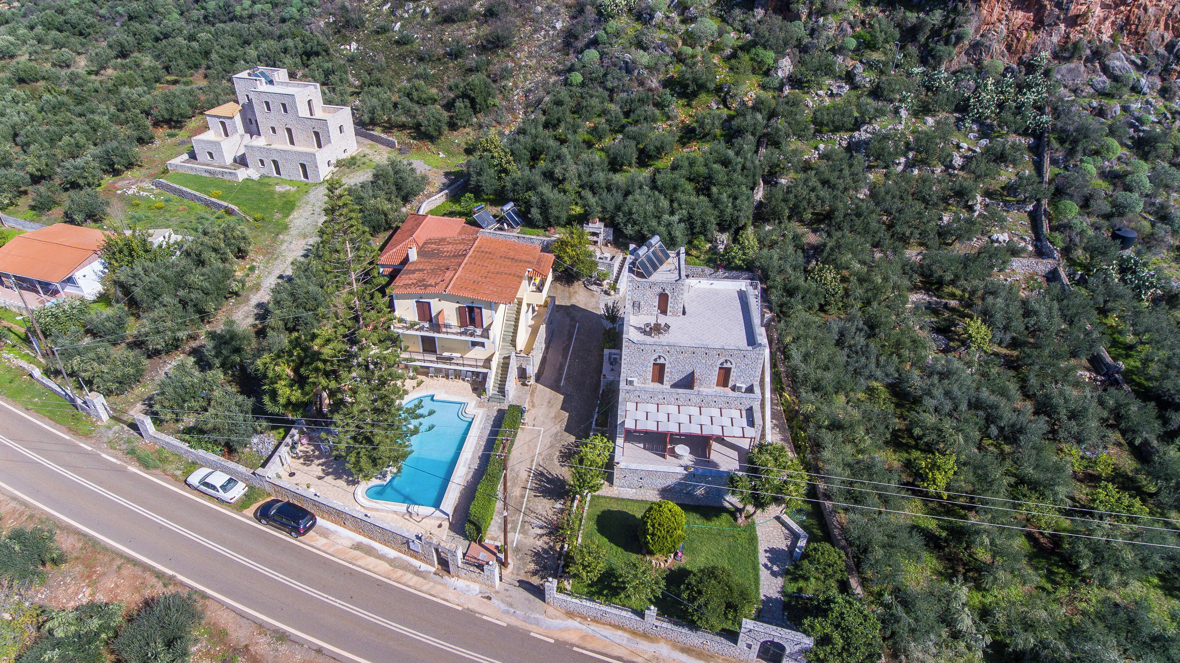 An aerial view of a property with a swimming pool, stone buildings, and a road nearby.