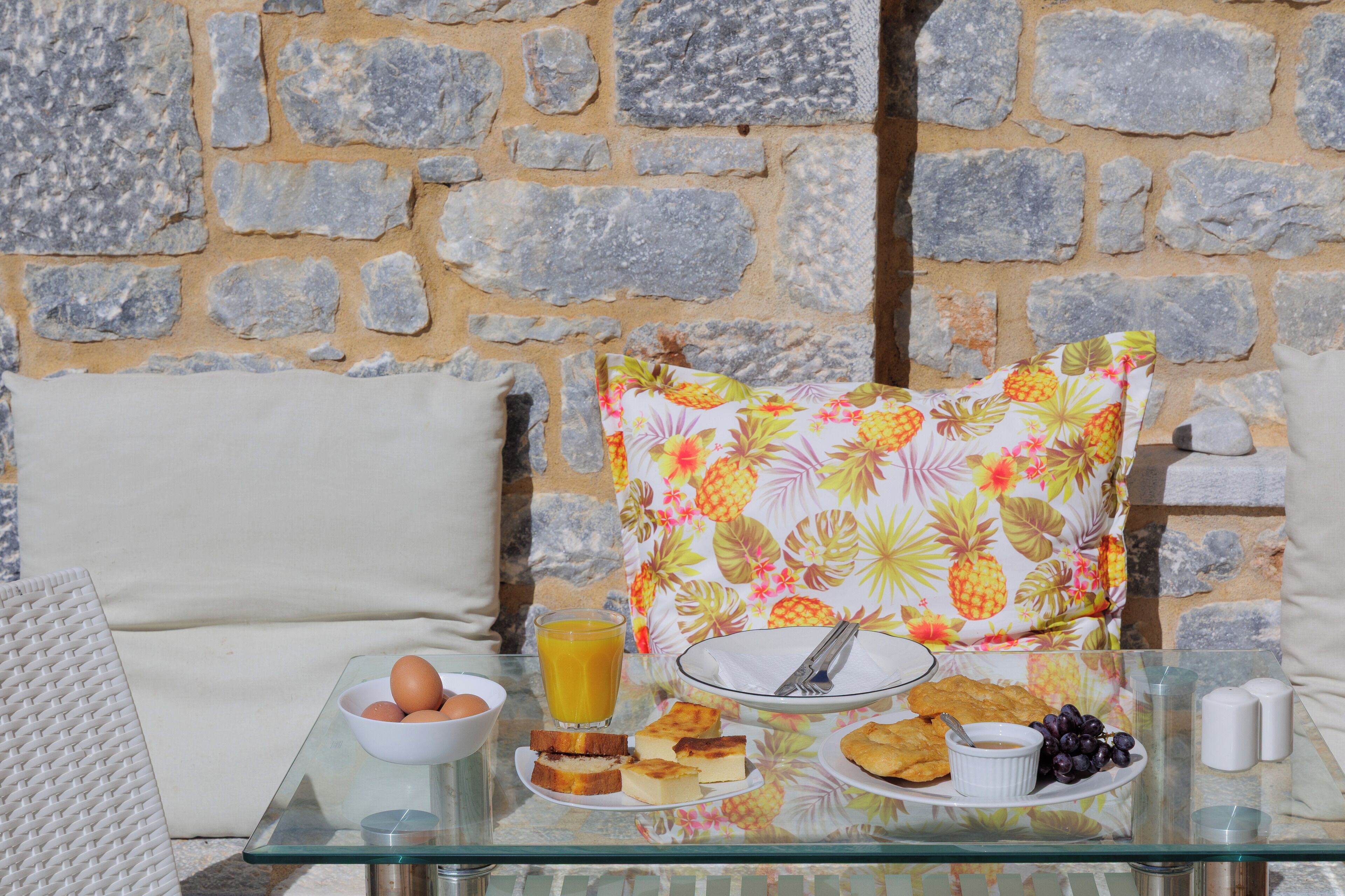 A breakfast table with eggs, toast, fruit, and juice against a stone wall.