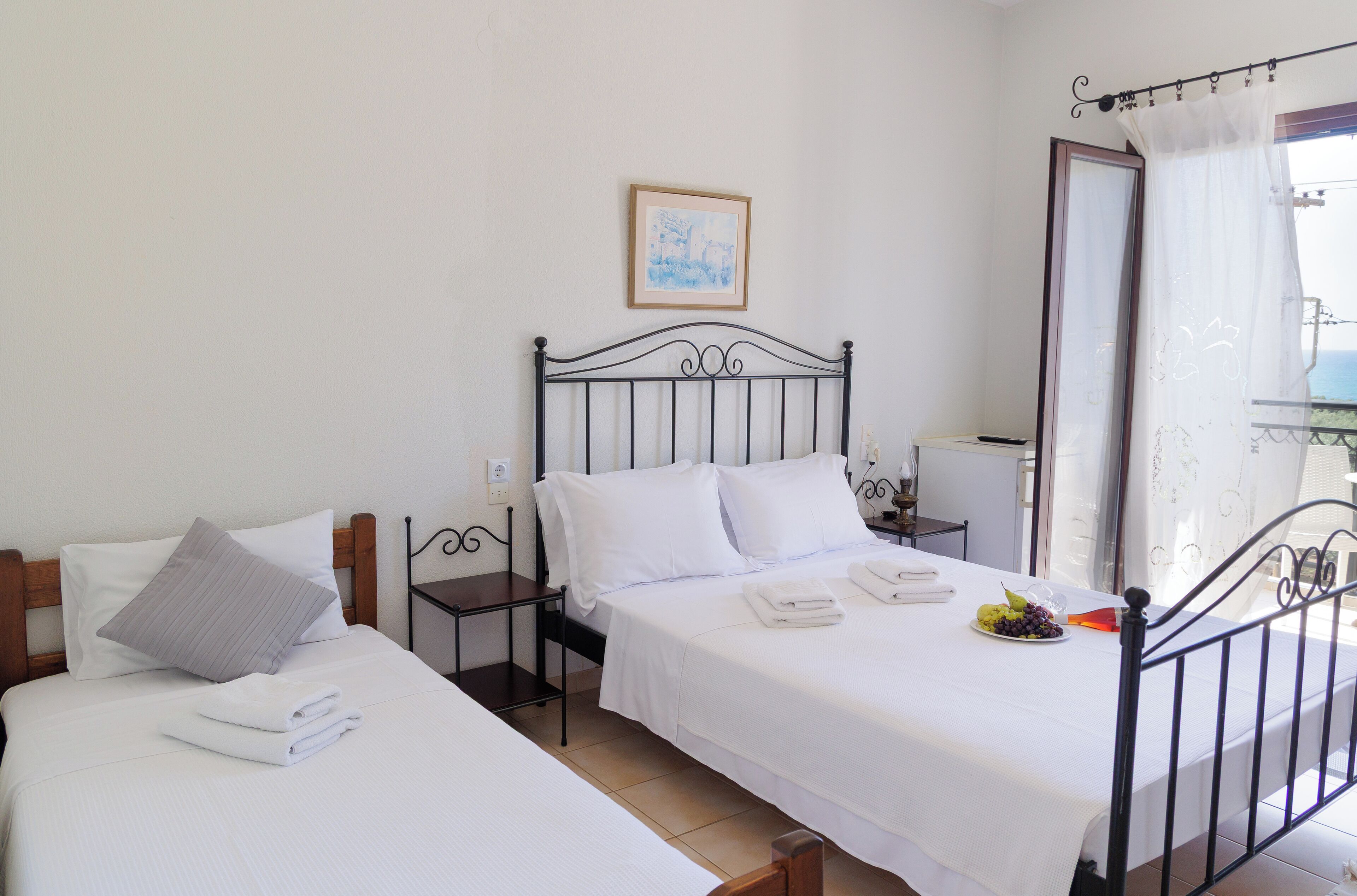 Habitación de hotel con dos camas, una mesita de noche con lámpara, un cuadro enmarcado en la pared y un balcón con vistas.