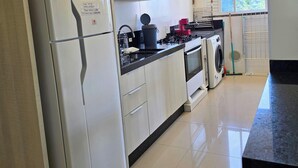 A kitchen with a refrigerator, stove, oven, and washing machine. - 3 minutes from the beach in the center of Bombinhas. Fully equipped apartment. (Bombinhas)