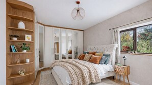Ein Schlafzimmer mit einem großen Bett, einem hölzernen Bücherregal, einem Spiegel und einem Fenster mit Blick auf Grünfläche.