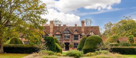 A historic building with a symmetrical facade, large windows, and a well-manicured garden.