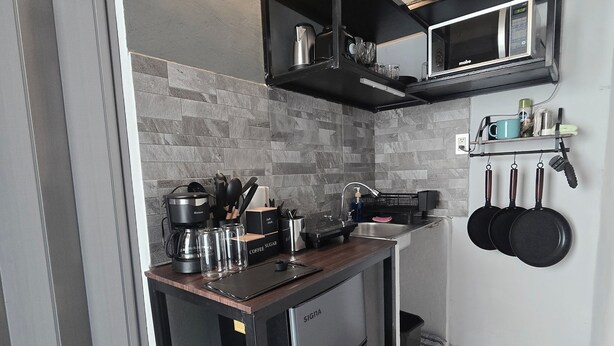 Una cucina compatta con frigorifero integrato, macchina da caffè e forno a microonde su un ripiano nero.