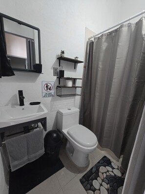 A bathroom with a white sink, a toilet, a shower curtain, and a sign prohibiting shoes. - A cozy loft designed especially for couples. (Ciudad de México)