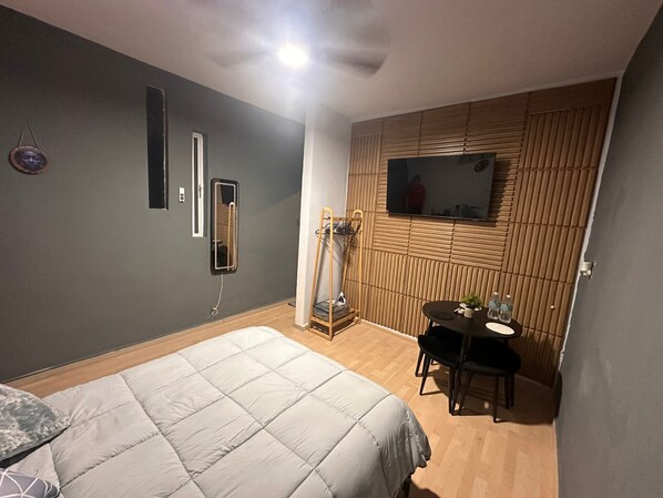 A bedroom with a bed, a small table with chairs, a TV mounted on the wall, and a mirror. - A cozy loft designed especially for couples. (Ciudad de México)