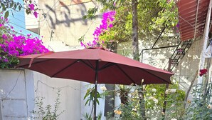 Un giardino con una fontana a più livelli, un ombrello rosso e diverse piante.