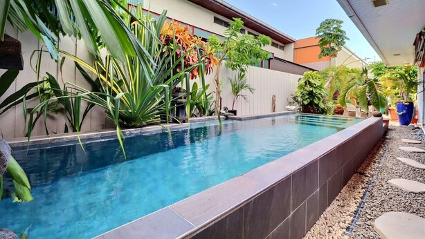 A swimming pool with a tiled edge, surrounded by various plants and a stone pathway. - Hiiaka room - city center - swimming pool (Papeete)