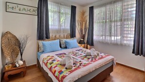 A neatly made bed with a colorful quilt, a bedside lamp, and a small table with a vase and a remote control. - Hiiaka room - city center - swimming pool (Papeete)