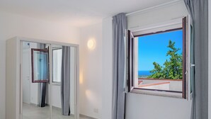 Et hotelværelse med et stort spejl, en skydedør og et vindue med udsigt til hav og grønne områder.