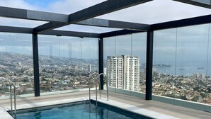 Ein Infinity-Pool auf dem Dach mit Blick auf die Stadt, umgeben von Glaswänden und Metallstreben.
