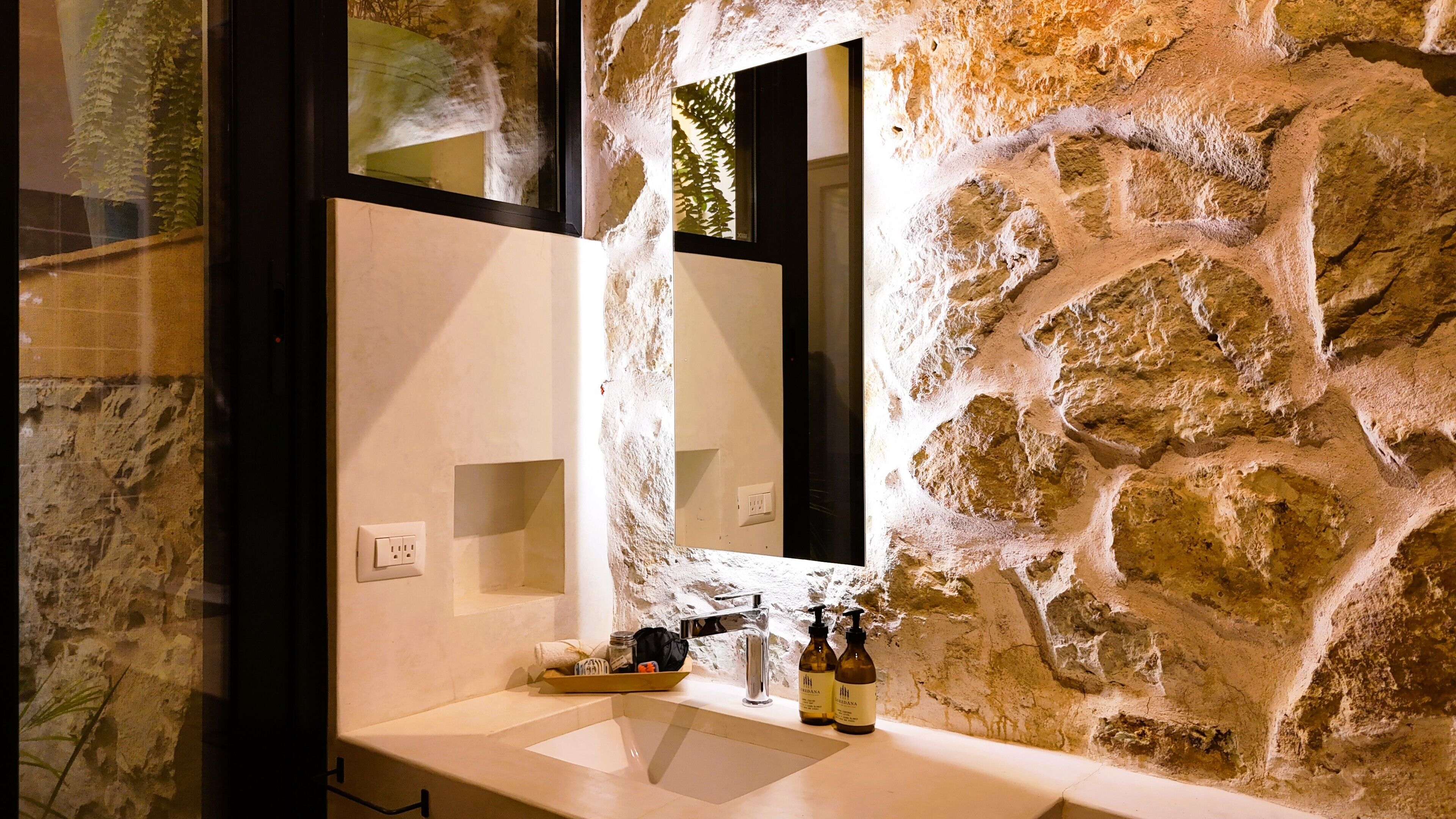 A bathroom with a stone wall, a sink, a mirror, and toiletries.