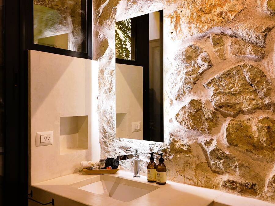 A bathroom with a stone wall, a sink, a mirror, and toiletries.