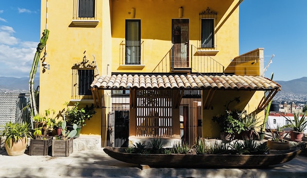 A yellow building with a tiled roof, a wooden fence, and potted plants. - El Diablo y La Luna B&B (Oaxaca)