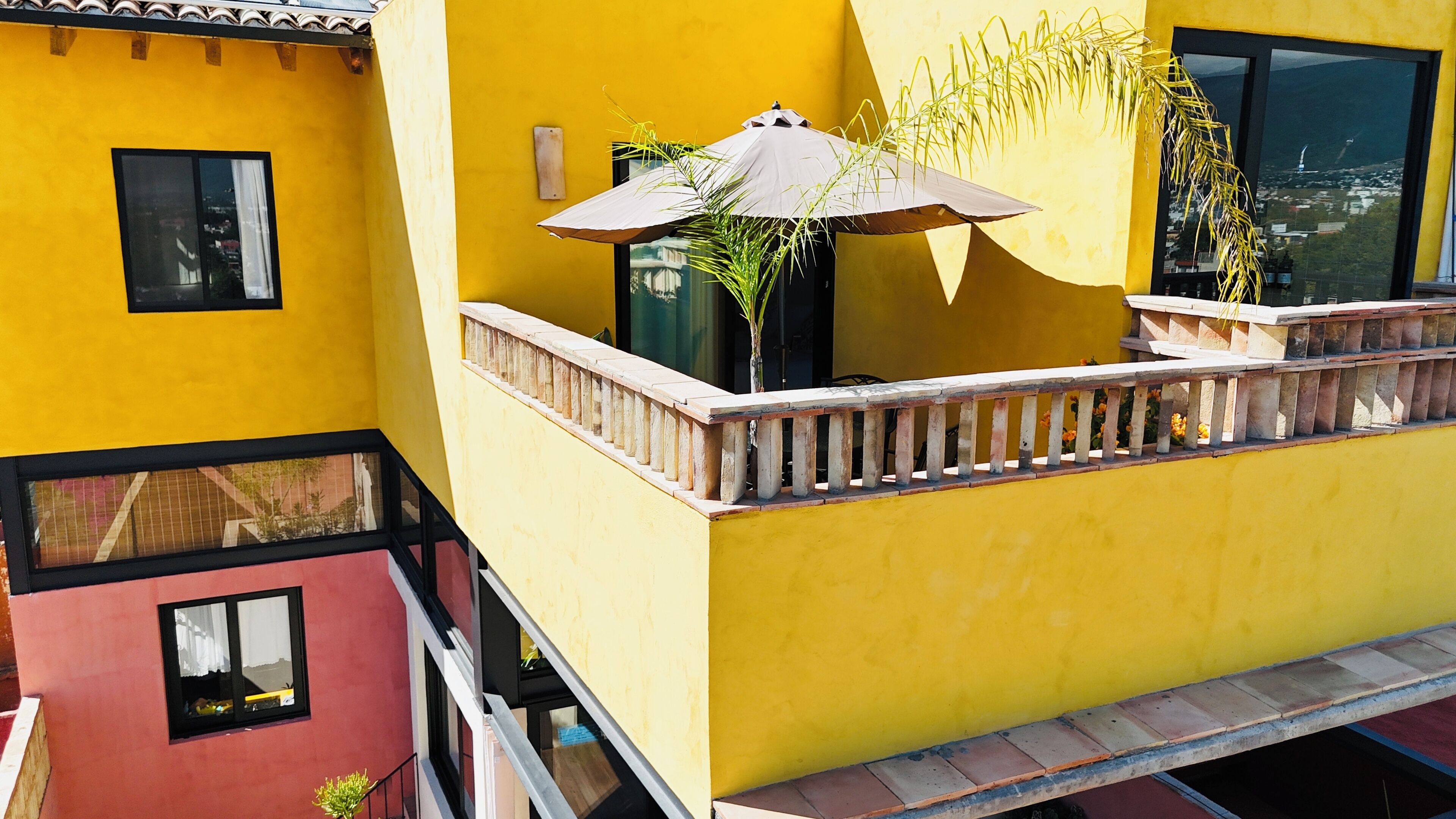 A yellow building with a balcony, a window, and a plant.