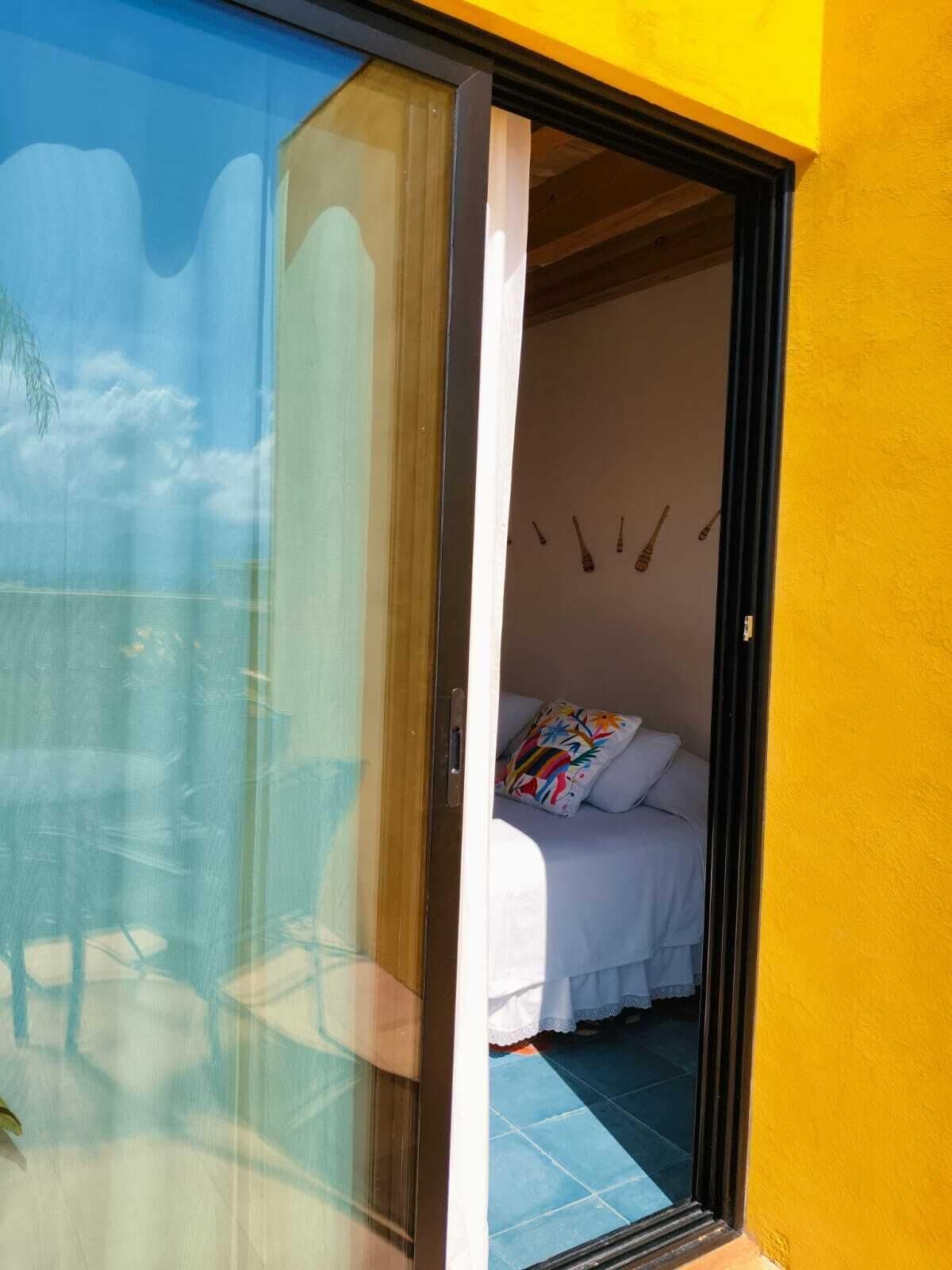 Una habitación con una cama, una almohada colorida y una ventana con vistas al cielo y nubes.
