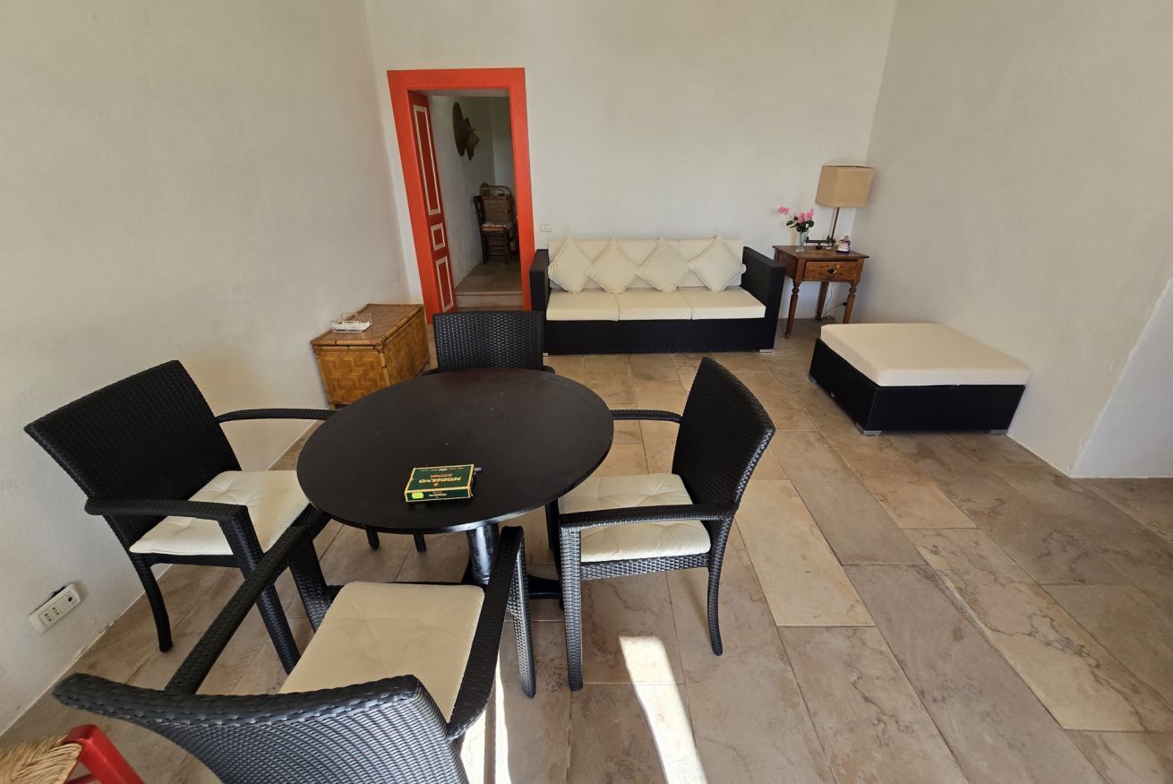 A living room with a round table, four chairs, a sofa, a small table with a lamp, and a bench.