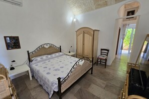 Una camera da letto con un letto, un armadio in legno, una sedia, una scrivania con una lampada e un quadro appeso al muro.