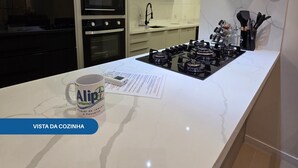 Ett modernt kök med en vit bänkskiva i marmor, en inbyggd ugn, en mikrovågsugn och en gasspis. På bänkskivan står en kaffemugg och på väggen hänger en meny.