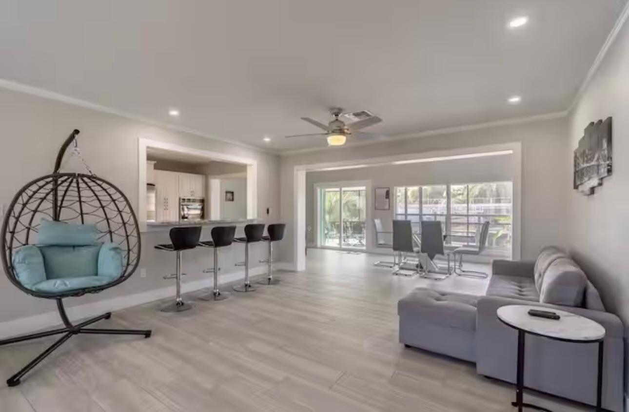 A modern living room with a hanging chair, a sofa, and a dining area with bar stools.