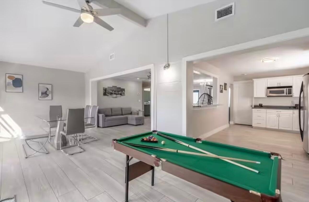 A modern living room with a pool table, a sofa, and a dining area.