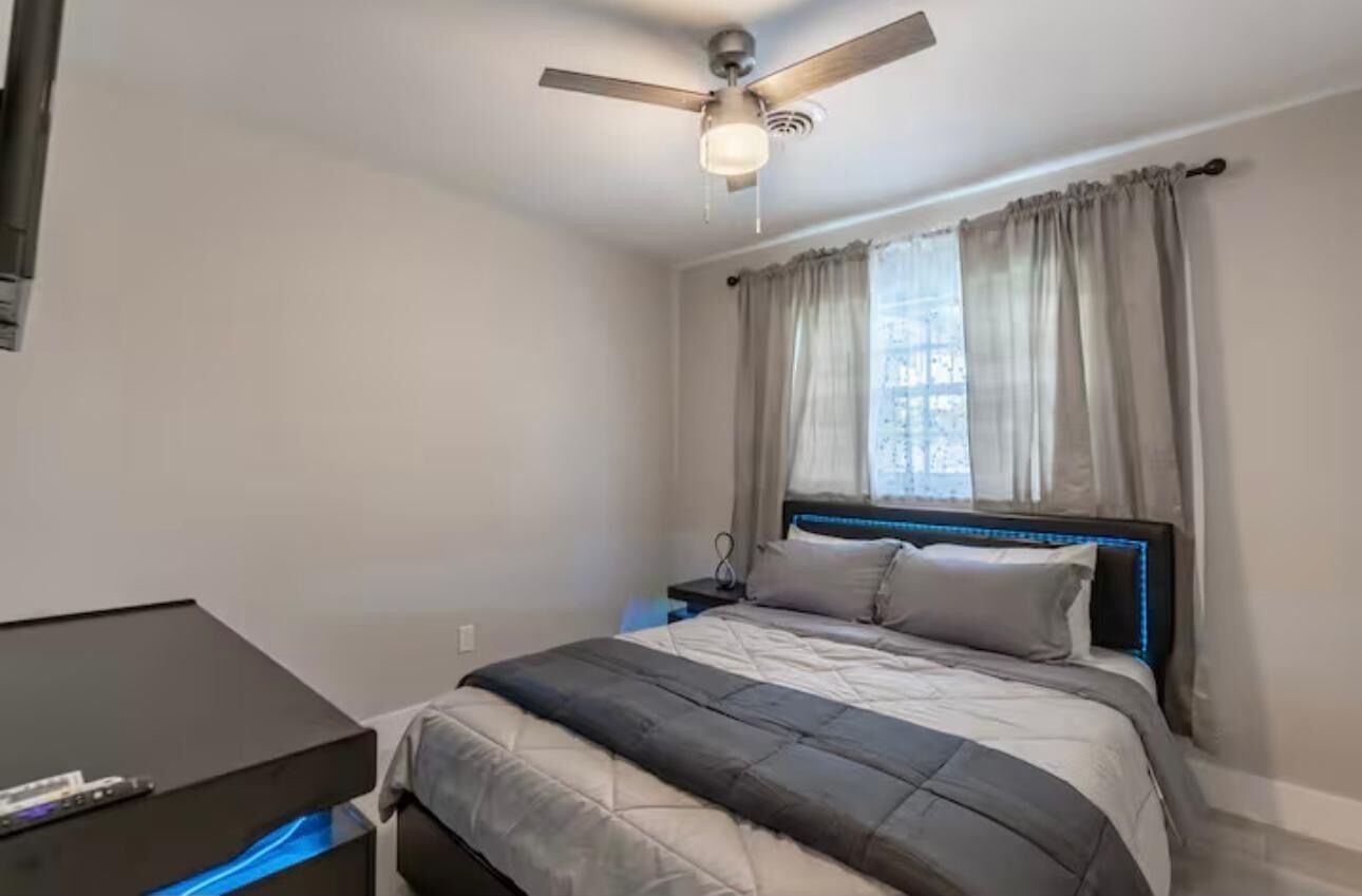Een slaapkamer met een bed, een plafondventilator, een nachtkastje en een bureau met een lamp.
