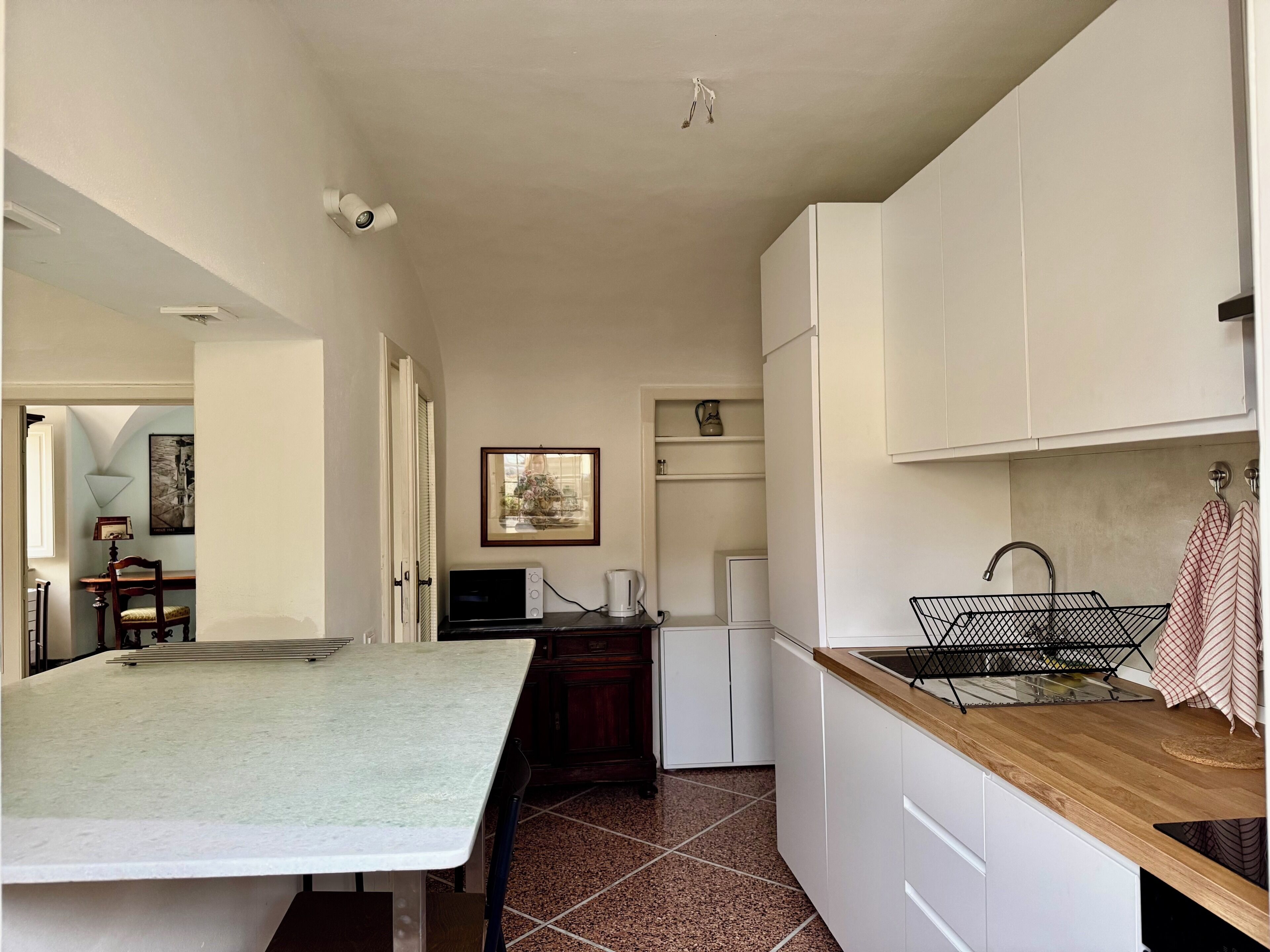 A compact kitchen with white cabinets, a wooden countertop, a sink, and a small refrigerator.