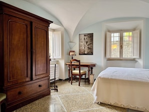 A bedroom with a bed, a wooden wardrobe, a desk with a chair, a window, and a framed picture on the wall. - Charming palazzetto in Calci (Calci)