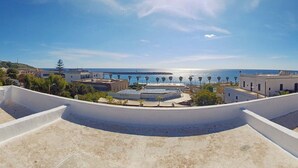 A rooftop terrace with a view of the sea, buildings, and a clear sky.