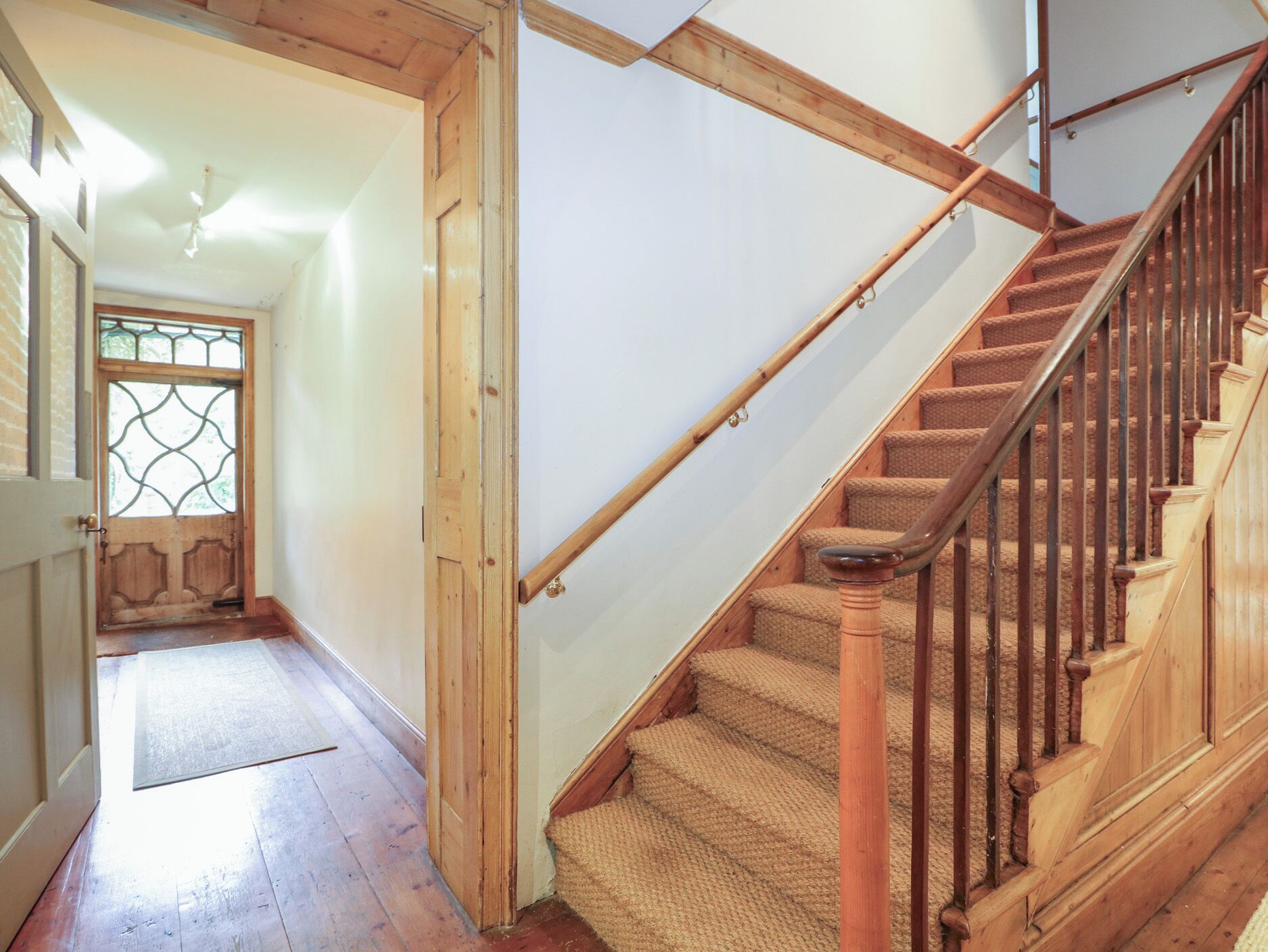 Un escalier en bois avec une rampe, des marches recouvertes de moquette et une porte en bois dotée d’une vitre.