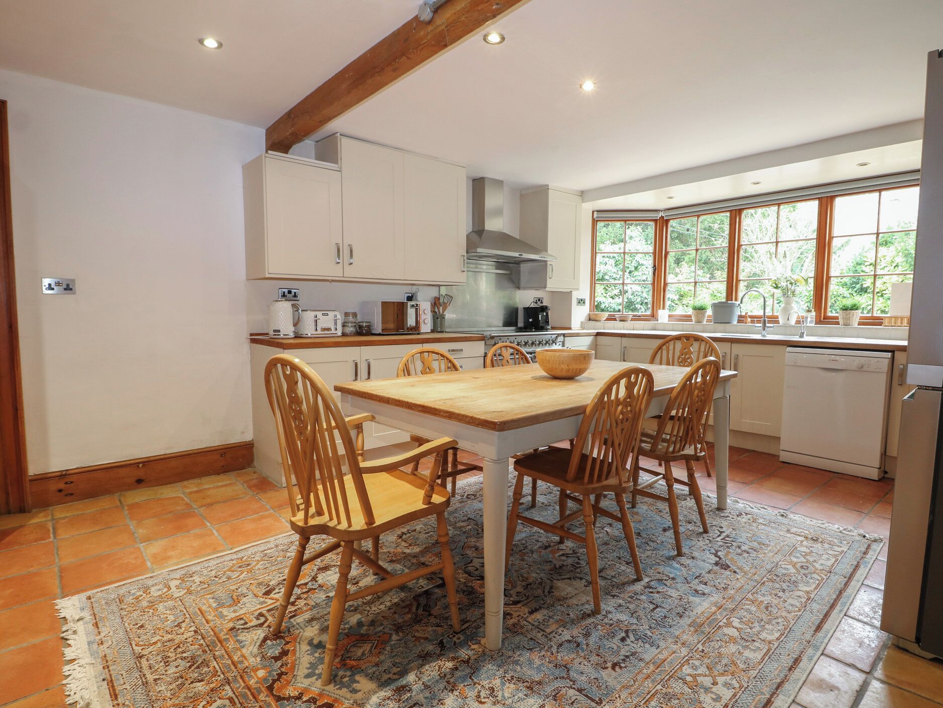 A kitchen with a wooden table and chairs, white cabinets, a stove, and a window with a view of greenery.