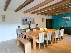 Uma área de refeições com mesa de madeira, cadeiras brancas, um banco e uma parede em tom de verde-água.