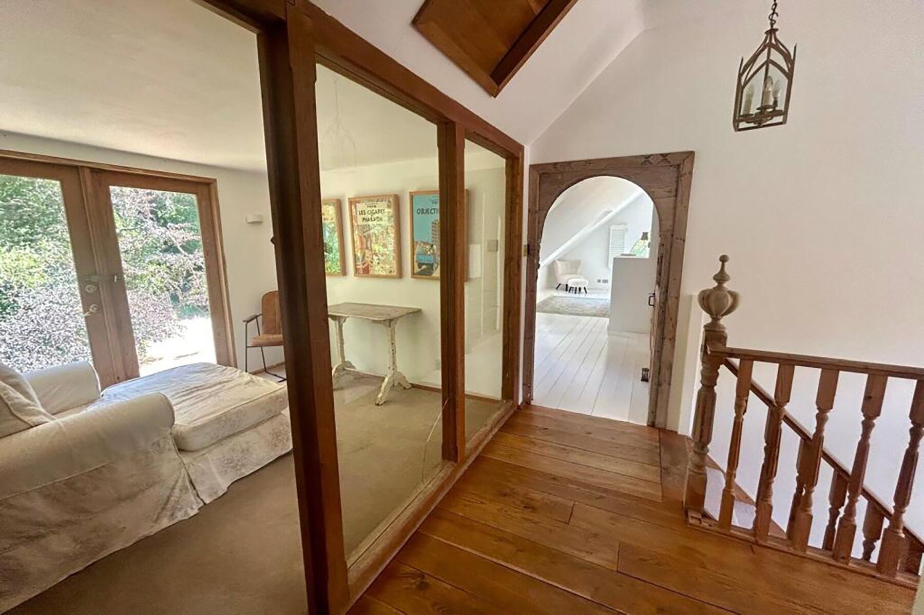 A wooden staircase leading to a second floor, a white sofa in a sunlit room, and a view of the outside through a glass door.