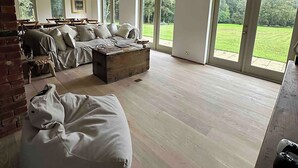 A spacious living room with a large sofa set, a coffee table, and a bean bag chair. There are large windows providing a view of a green landscape. - Elegant Hampshire Countryside Stay, Petersfield (Petersfield)