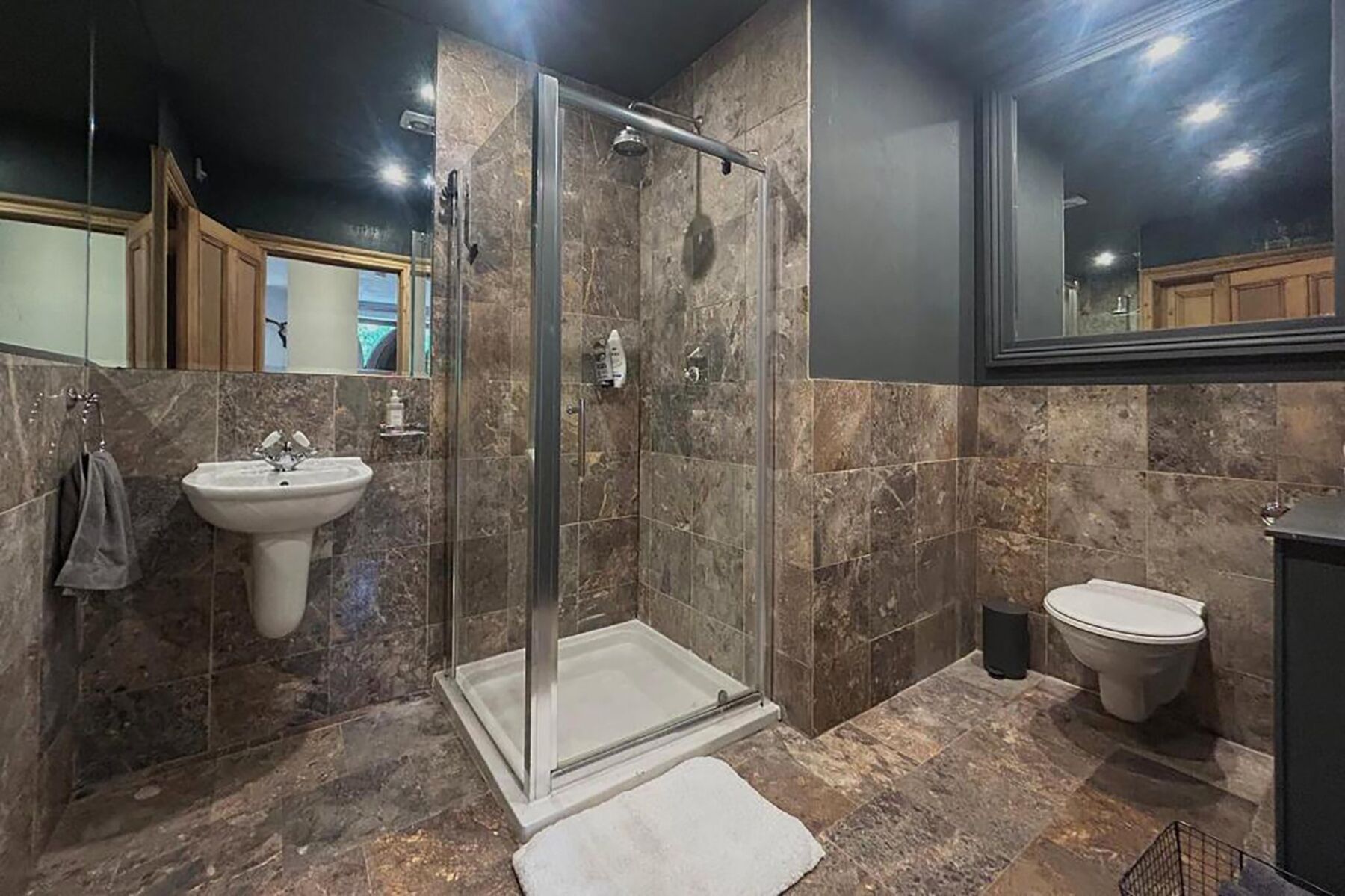 A modern bathroom with a glass-enclosed shower, a pedestal sink, and a toilet.