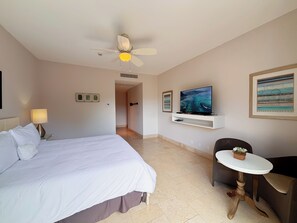 Ein Hotelzimmer mit Bett, Schreibtisch, Stuhl, Fernseher und Deckenventilator.