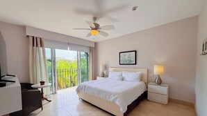 A hotel room with a bed, bedside tables, a desk, a ceiling fan, and a view of greenery outside. - Tropical Garden Retreat 2BR in Plaza Puntarena (Río Hato)
