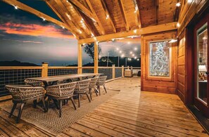 A wooden deck with a table and chairs, a glass door, and a view of the landscape. - New Luxury Design, 5mi to Parkway, Sauna, Hot Tub! (Sevierville)