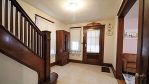 Una escalera de madera lleva a un rellano con suelo de baldosas, un armario de madera y una puerta con ventana.