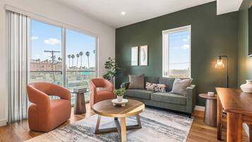 A modern living room with a green accent wall, a sofa, two armchairs, a coffee table, and a dining table.